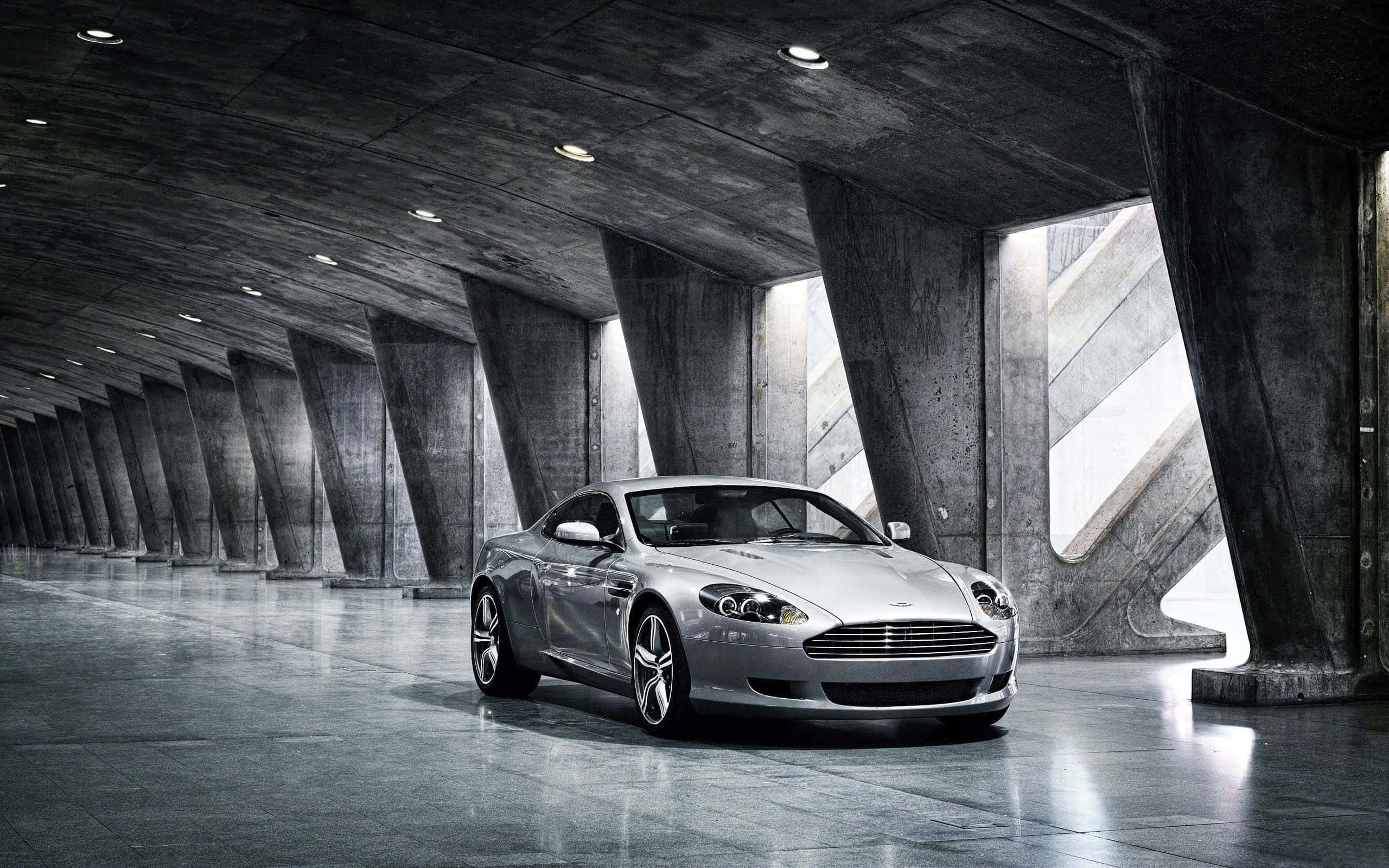 Aston Martin DB9 na Naglalayag sa Isang Scenic Cityscape Wallpaper