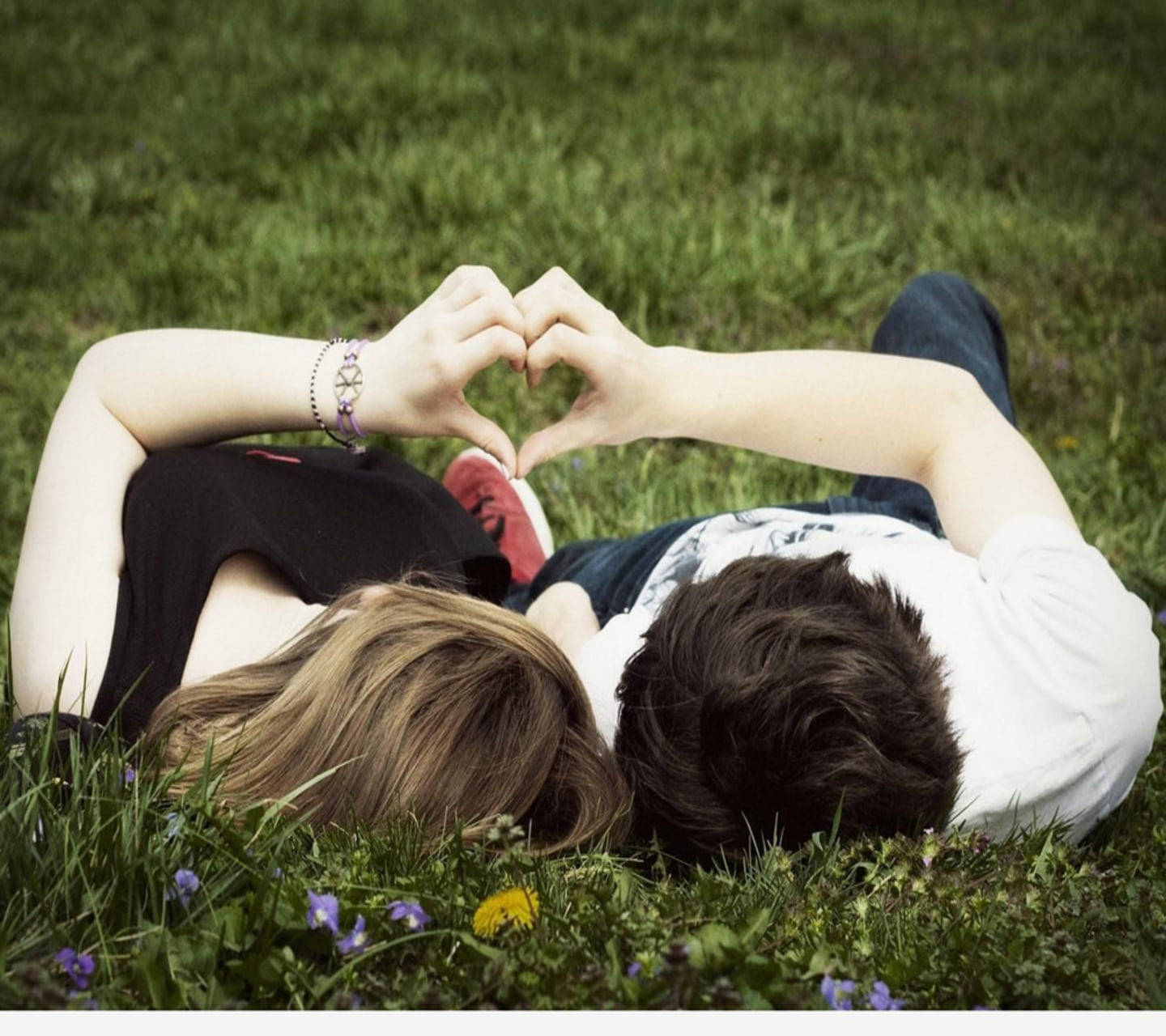Cute Couple na Gumagawa ng Cute Heart sa Damuhan Wallpaper