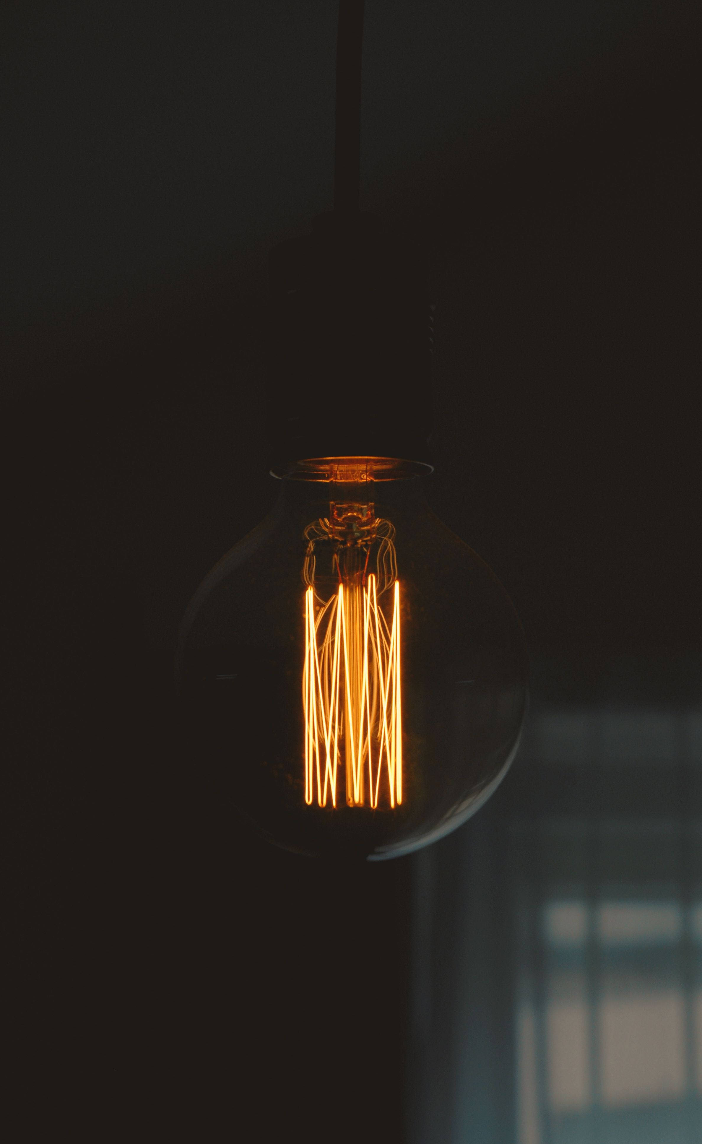 Iluminadong OLED Bombilya Laban sa Isang Madilim na Background sa Isang iPhone. Wallpaper