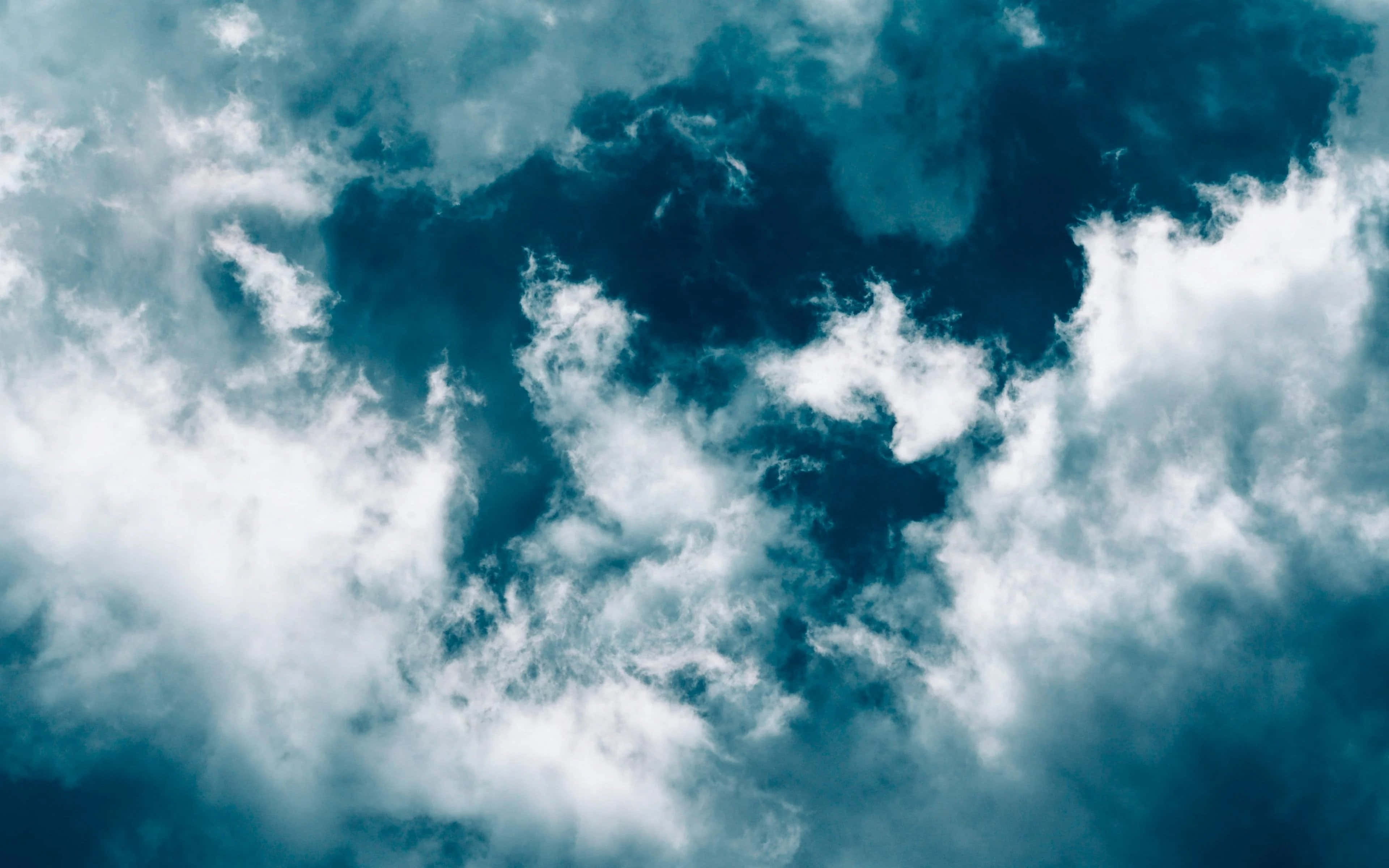 isang asul na langit na may mga ulap at isang eroplanong lumilipad sa ibabaw nito Wallpaper