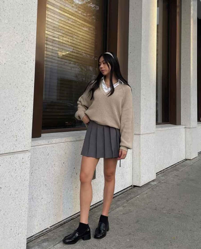 isang babaeng naka-sweater at palda na nakatayo sa tabi ng pader Wallpaper