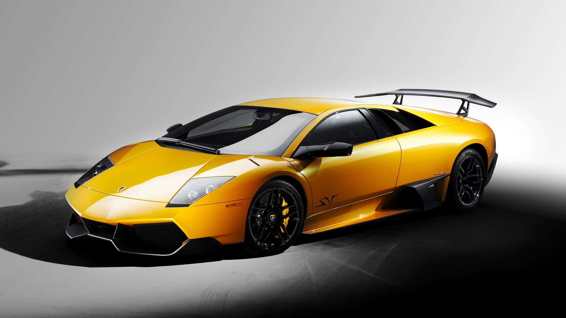 Isang dilaw na sports car ang ipinapakita sa isang madilim na silid Wallpaper