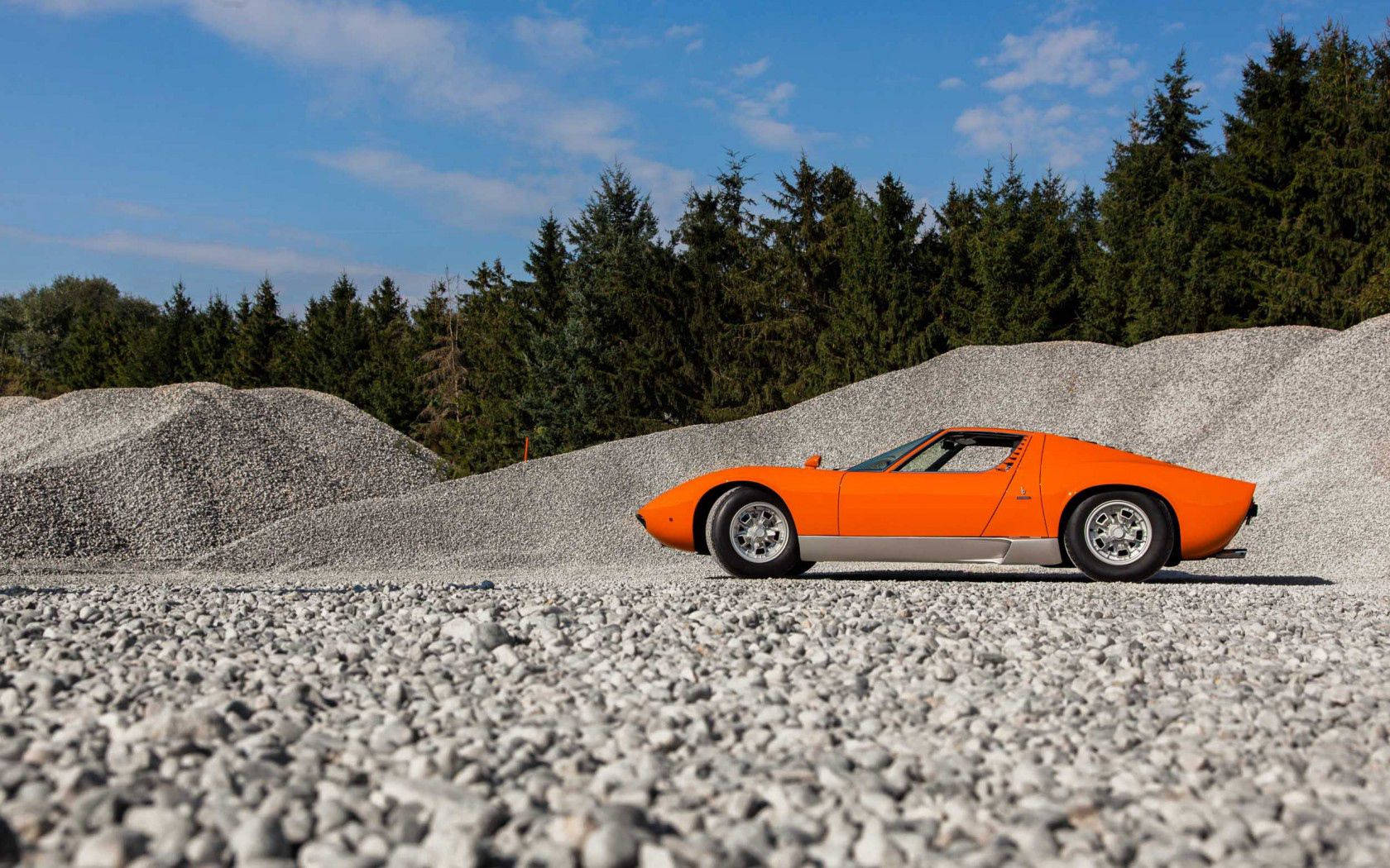 Isang katangi-tanging orange na Lamborghini Miura sa isang gravel road. Wallpaper