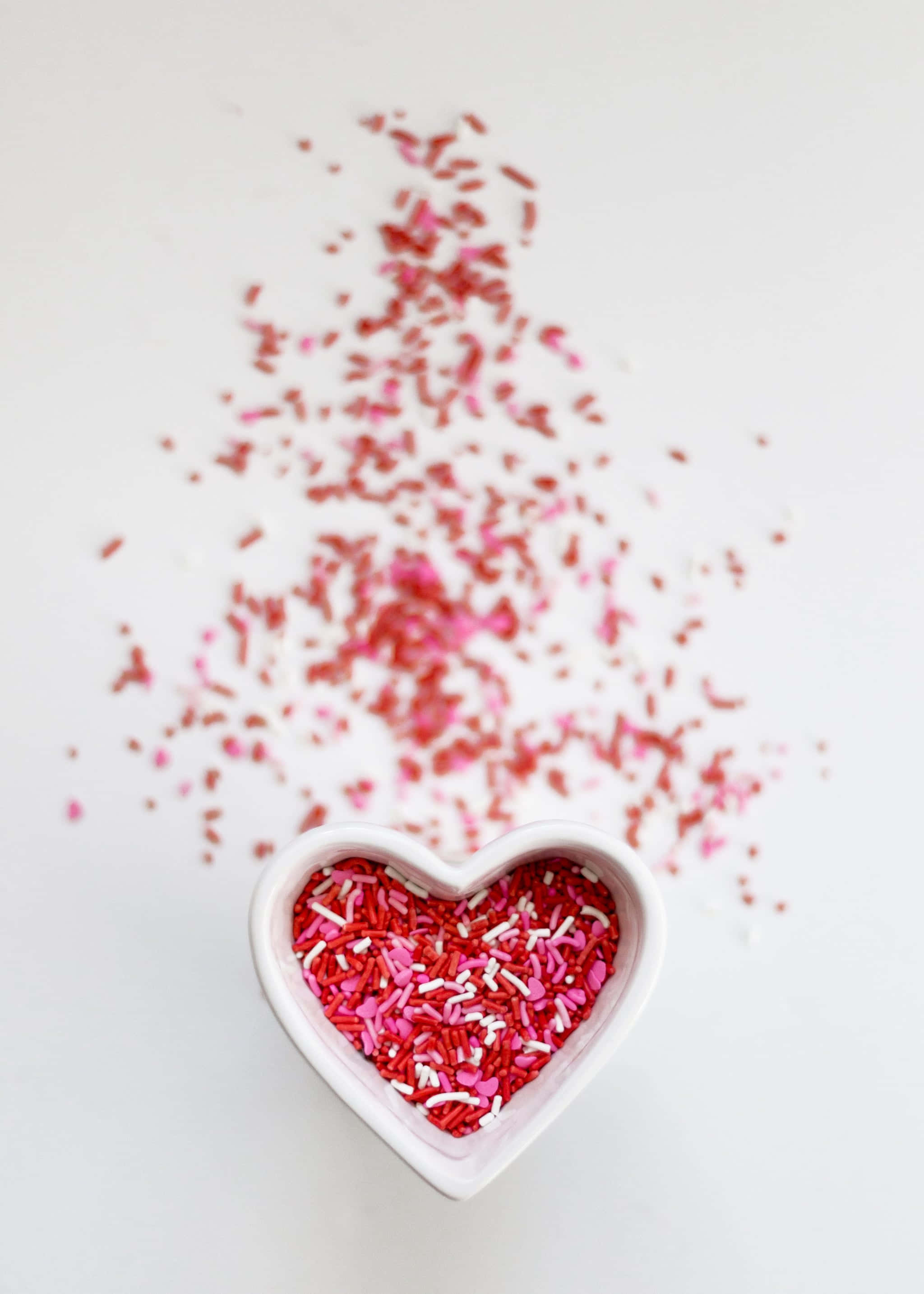 isang mangkok na hugis puso na puno ng pink at pulang confetti Wallpaper