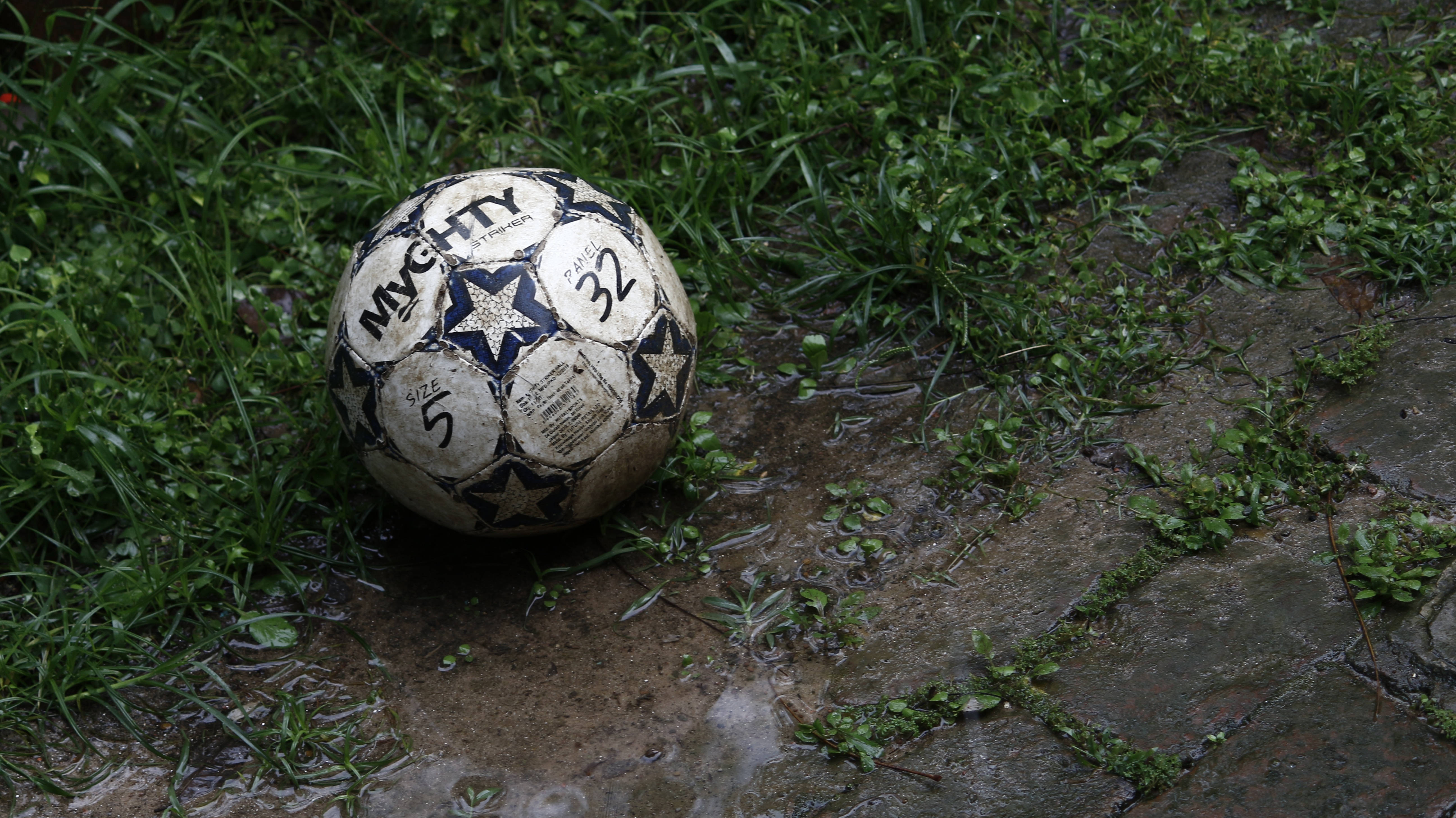 Isang maputik na football ang naiwang walang nag-aangkin sa damuhan. Wallpaper