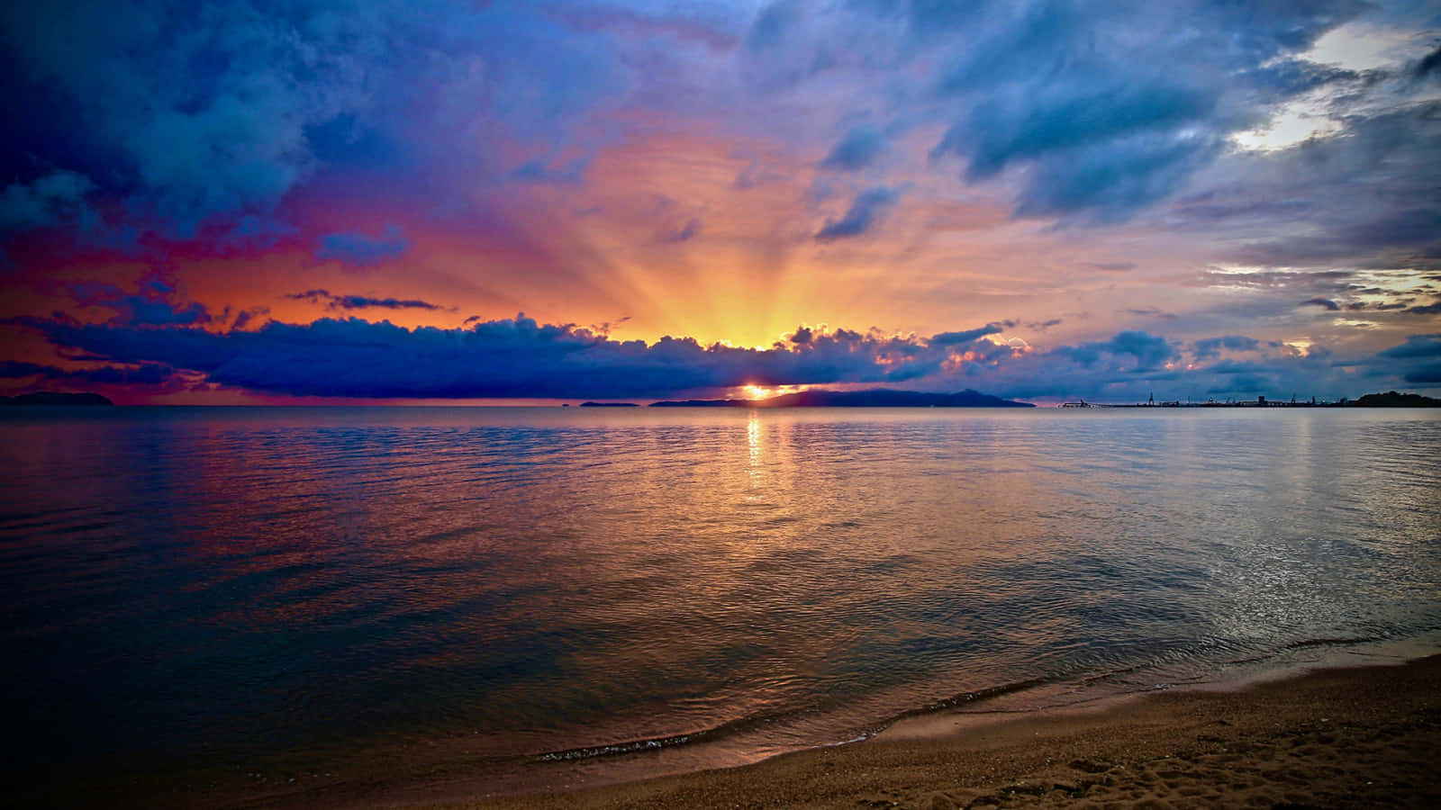 Isang nakamamangha na paglubog ng araw sa dalampasigan na tan-aw gikan sa layo Wallpaper