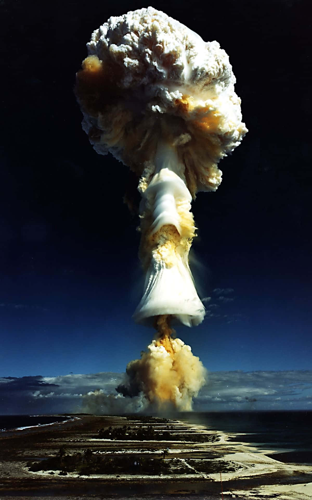 isang nuclear explosion ay nakikita sa itaas ng isang beach Wallpaper
