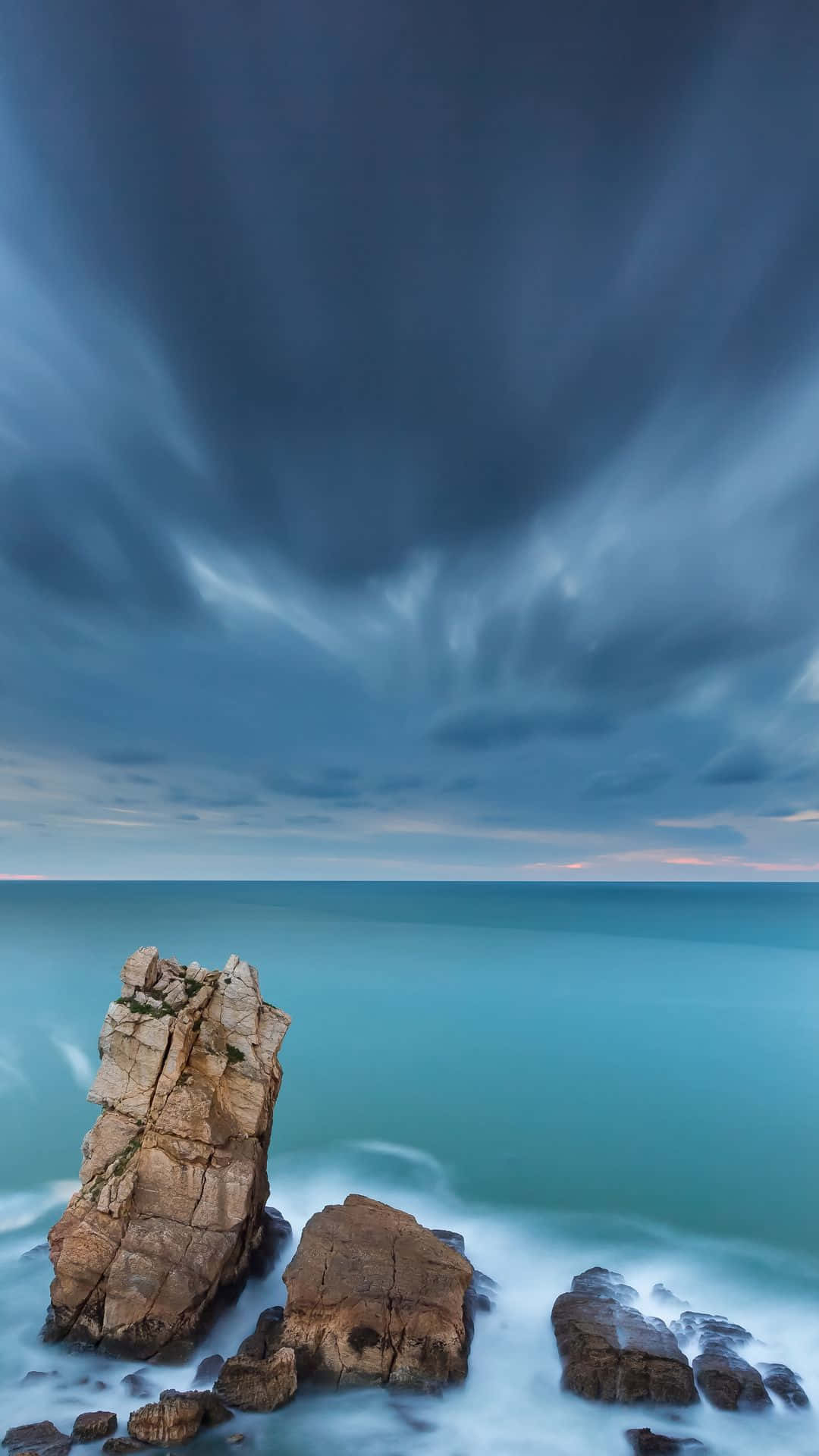 isang pormasyon ng bato na may madilim na langit at karagatan Wallpaper