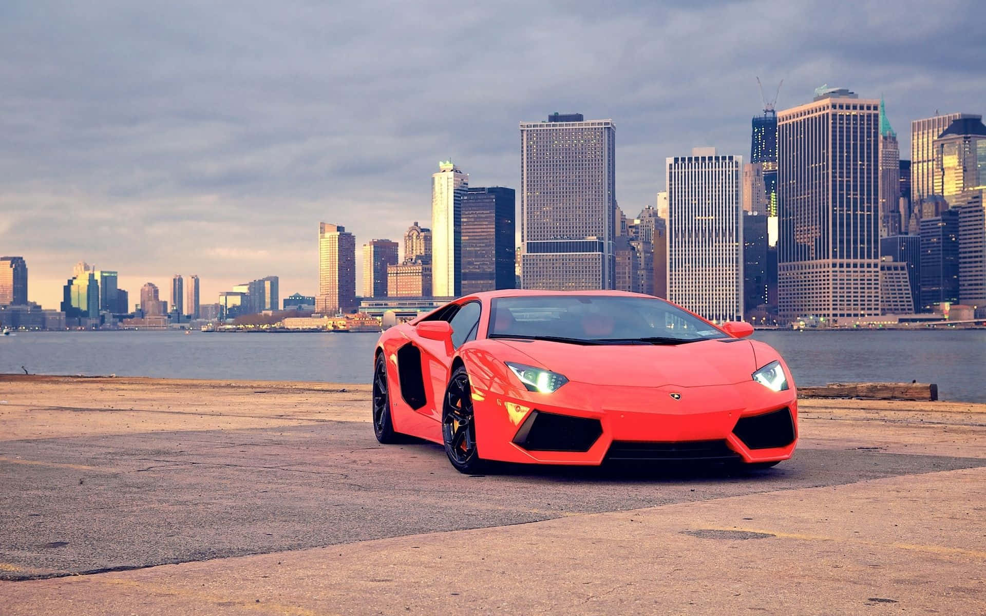 isang pulang sports car na nakaparada sa harap ng isang lungsod Wallpaper