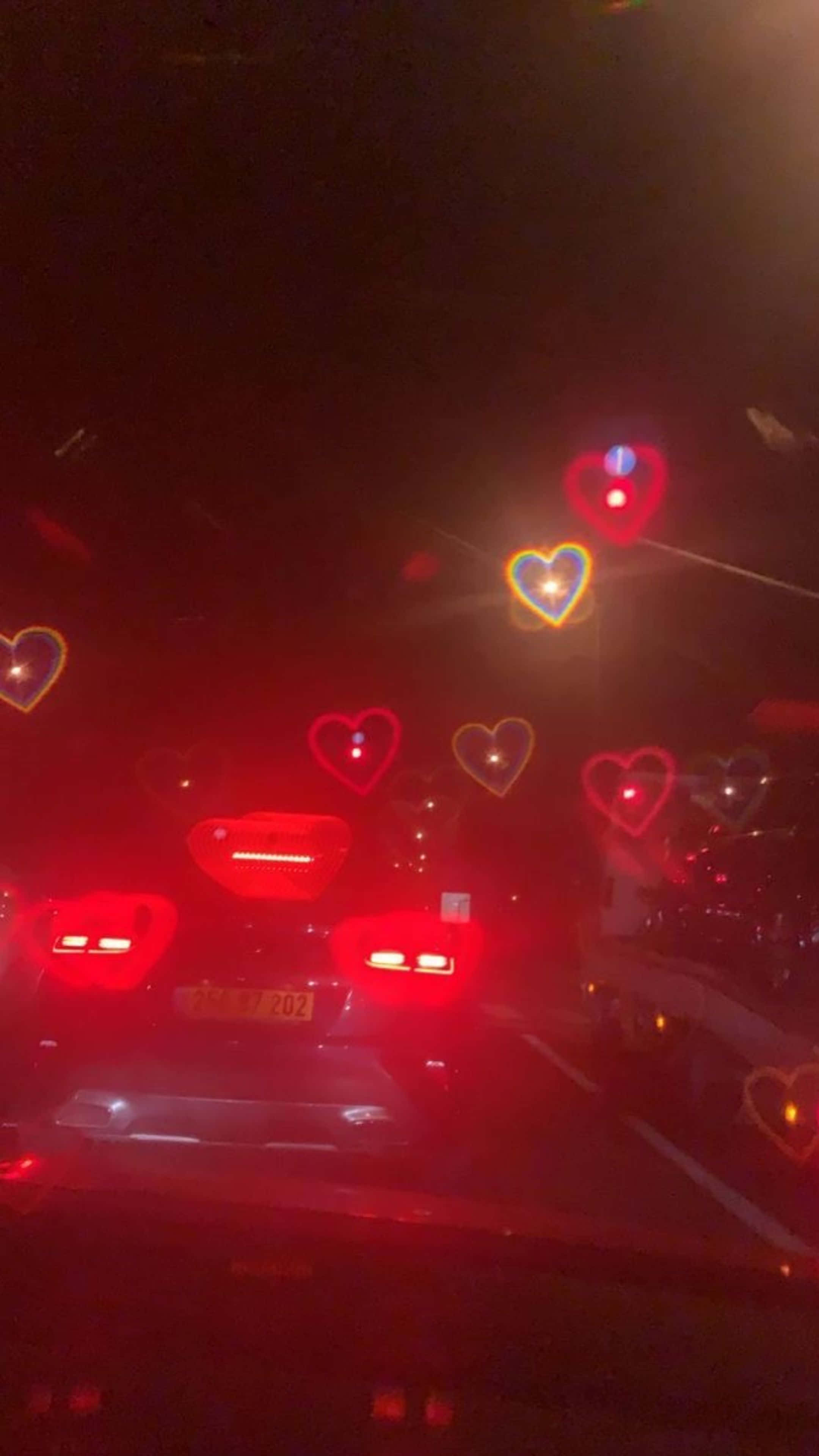 isang sasakyan na bumabiyahe sa kalsada sa gabi na may mga puso sa windshield Wallpaper