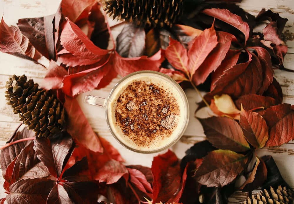 isang tasa ng kape na napapaligiran ng mga dahon at pine cone Wallpaper