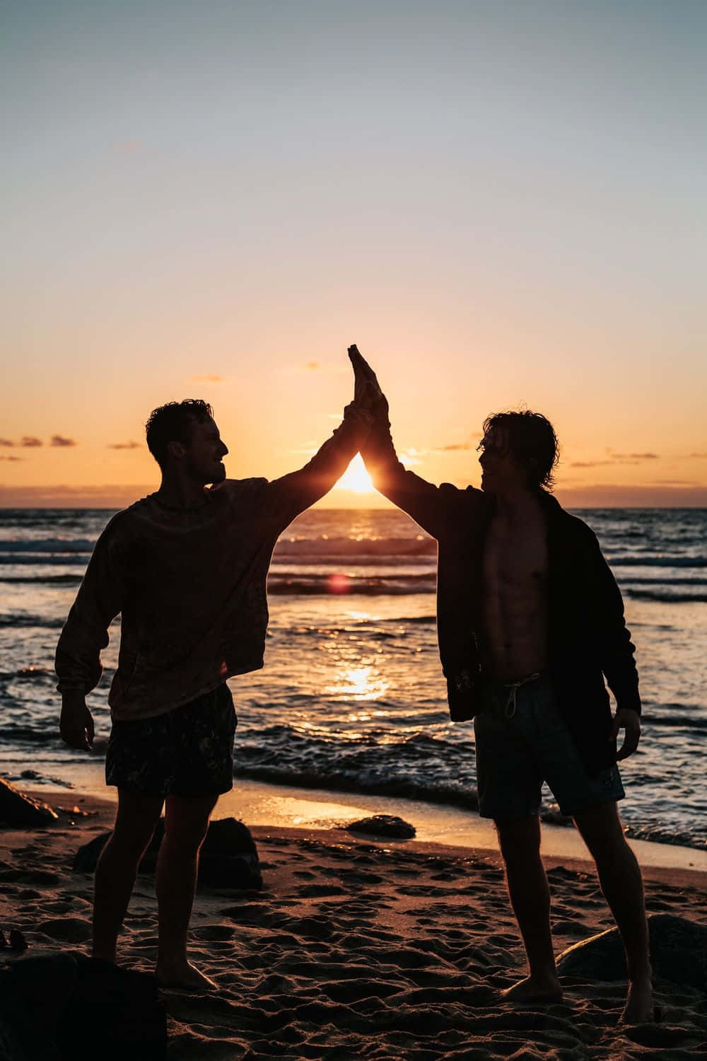 Larawan ng High Five ng Magkakaibigan sa Dalampasigan sa Paglubog ng Araw Wallpaper