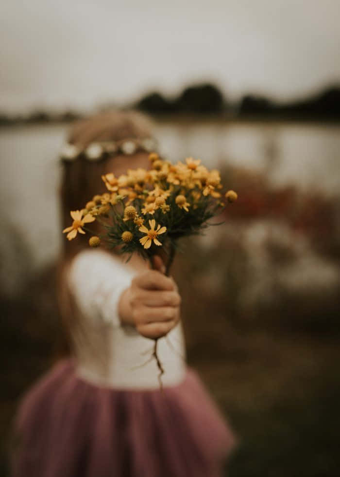 Larawan ng Isang Batang Babae na May Hawak na Dilaw na Bulaklak Wallpaper