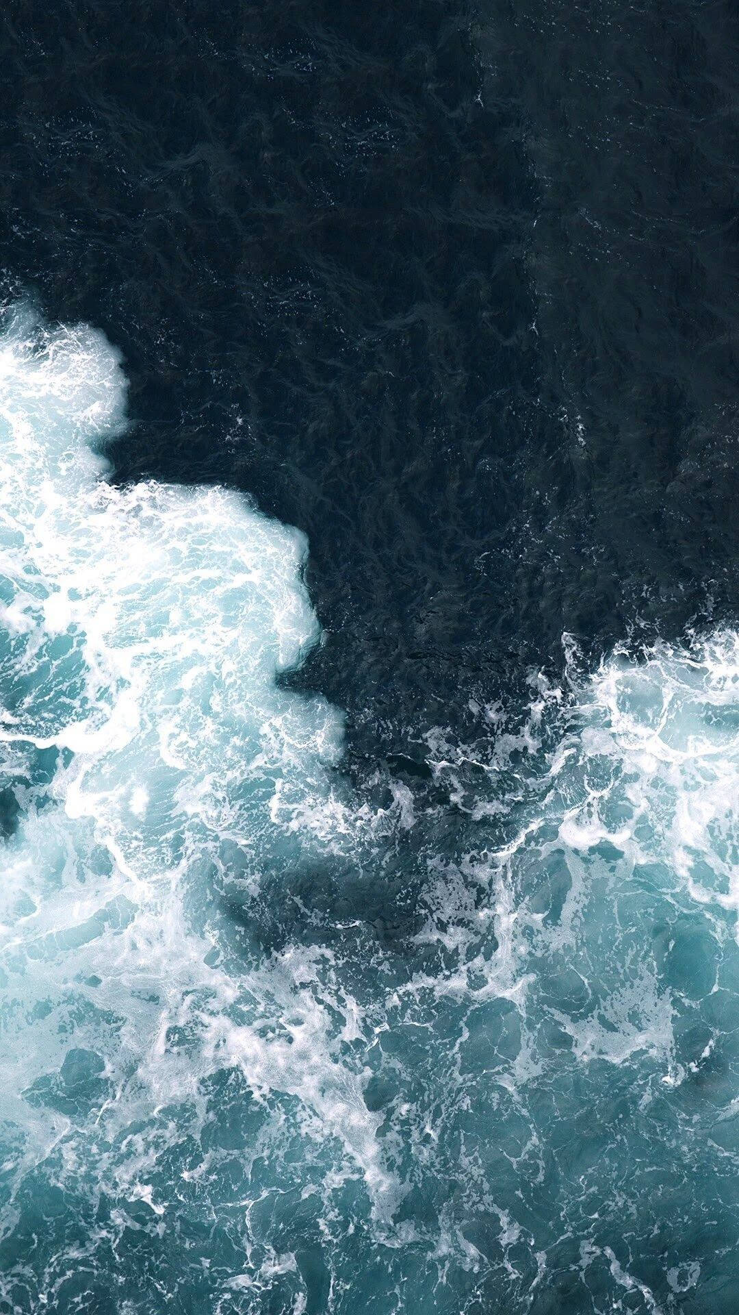 Tanawin mula sa itaas ng lakas ng mga alon ng karagatan na humahampas sa dalampasigan Wallpaper