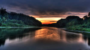 Calm river in jungle under orange sunset sky wallpaper