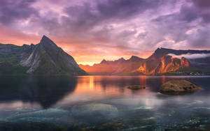 Lake at mountain range na may break of dawn clouds MacBook Pro wallpaper.