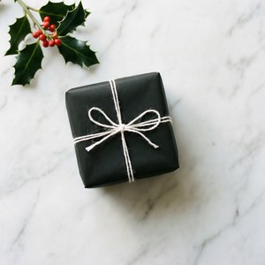 Simpleng itim at puting na regalo na may holly sa ibabaw ng marmol.