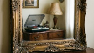 Isang makasaysayang salamin na may detalyadong disenyo na sumasalamin sa maaliwalas at retro na loob ng bahay.