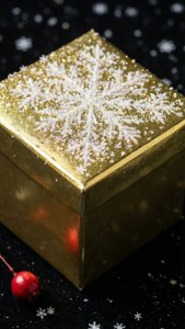 Makintab na regalong ginto na may mga snowflake sa itim na ibabaw kasama ang berry.