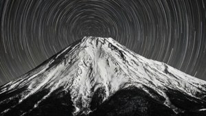 Isang long exposure black and white na larawan ng mga bakas ng bituin na umiikot sa isang bundok na may niyebe.